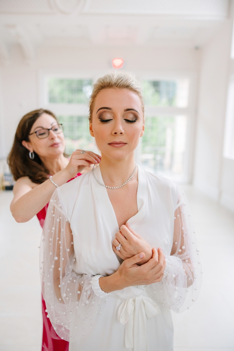 Bride in a white robe getting a necklace put on by stylist