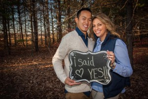 Tom and Diana in a forest, holding up a sign that reads "I said yes"